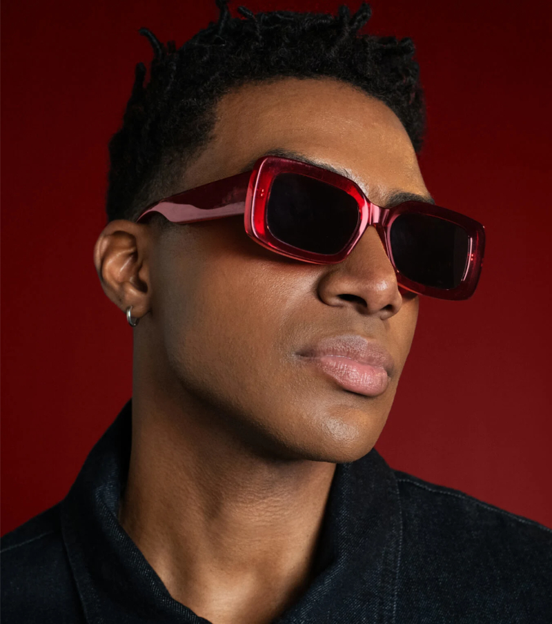 Man modeling cherry red sunglasses against a deeper red background. 