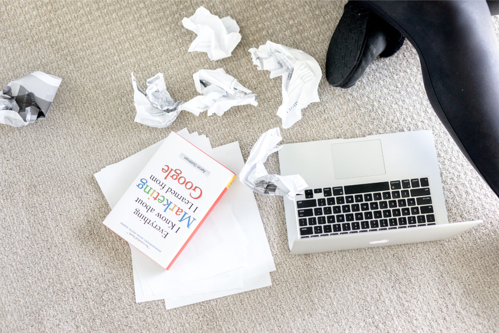 Top view of a laptop with crumbled papers nearby and the book "Everything I know about marketing I learned from Google."