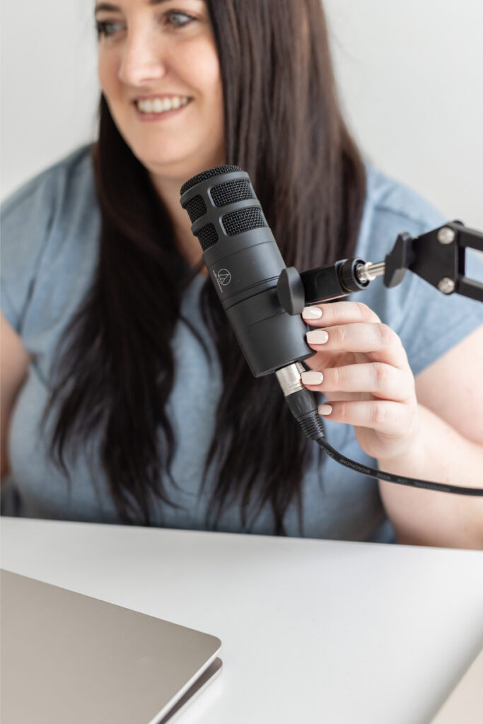 Kara records with microphone as she discusses growing your podcast with Pinterest and blog content.